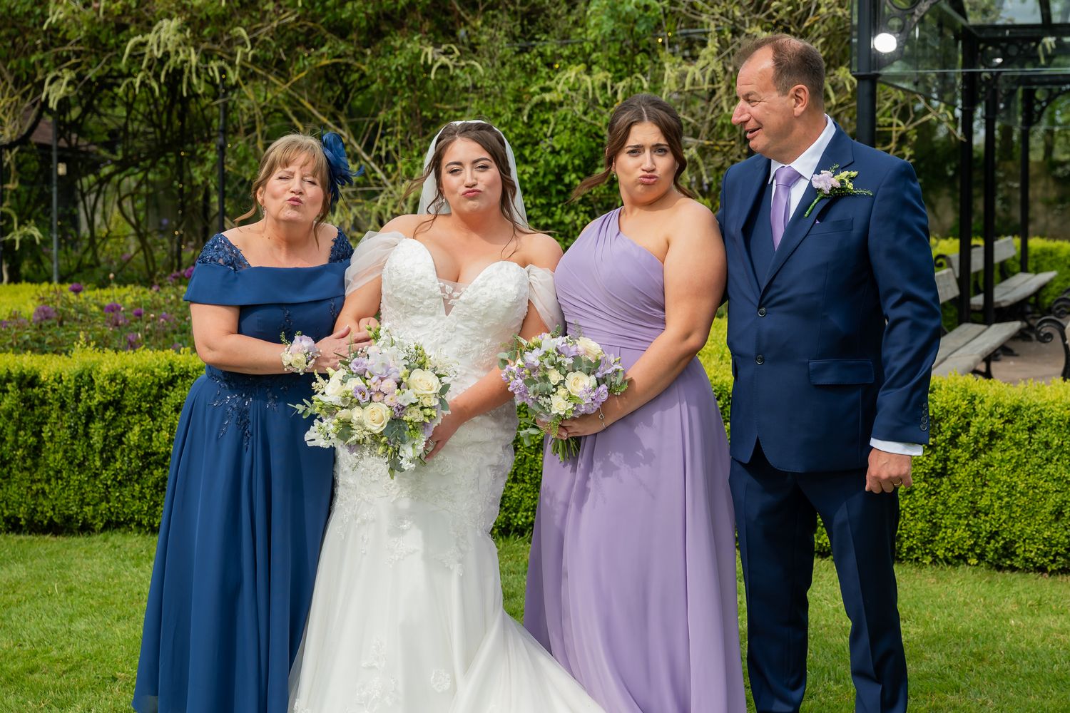 Bride in white gown with bridesmaid and parents posing outdoors at a garden wedding ceremony.