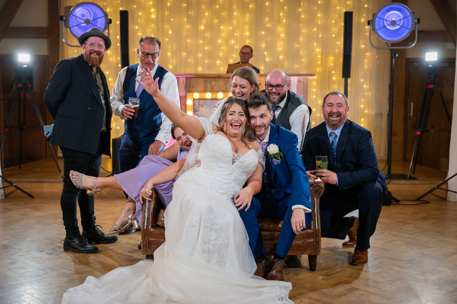 Bride and groom celebrate with wedding party guests on dance floor with fairy lights in rustic barn venue.