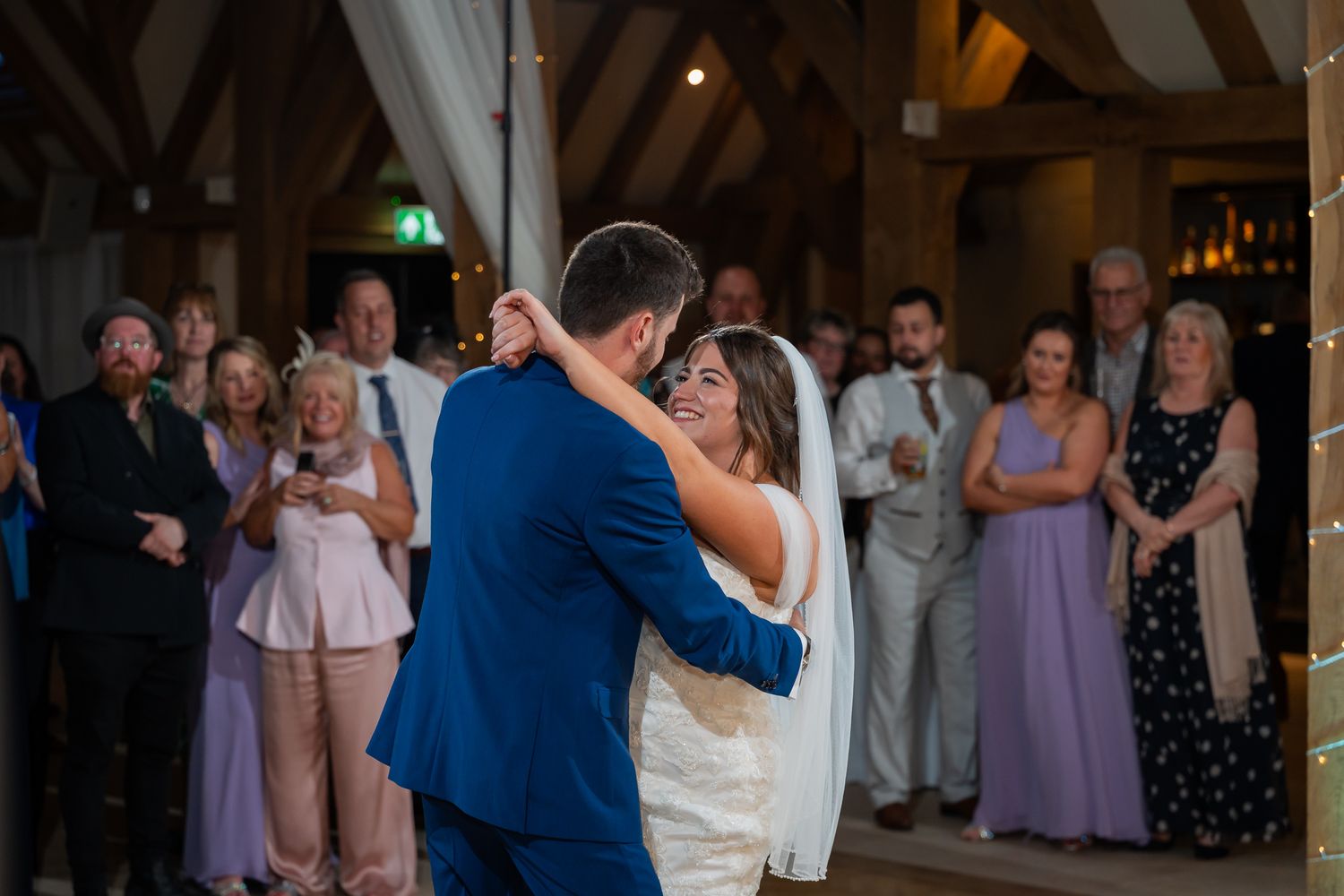 Bride and groom share their first dance at a rustic barn wedding reception while guests watch and celebrate.