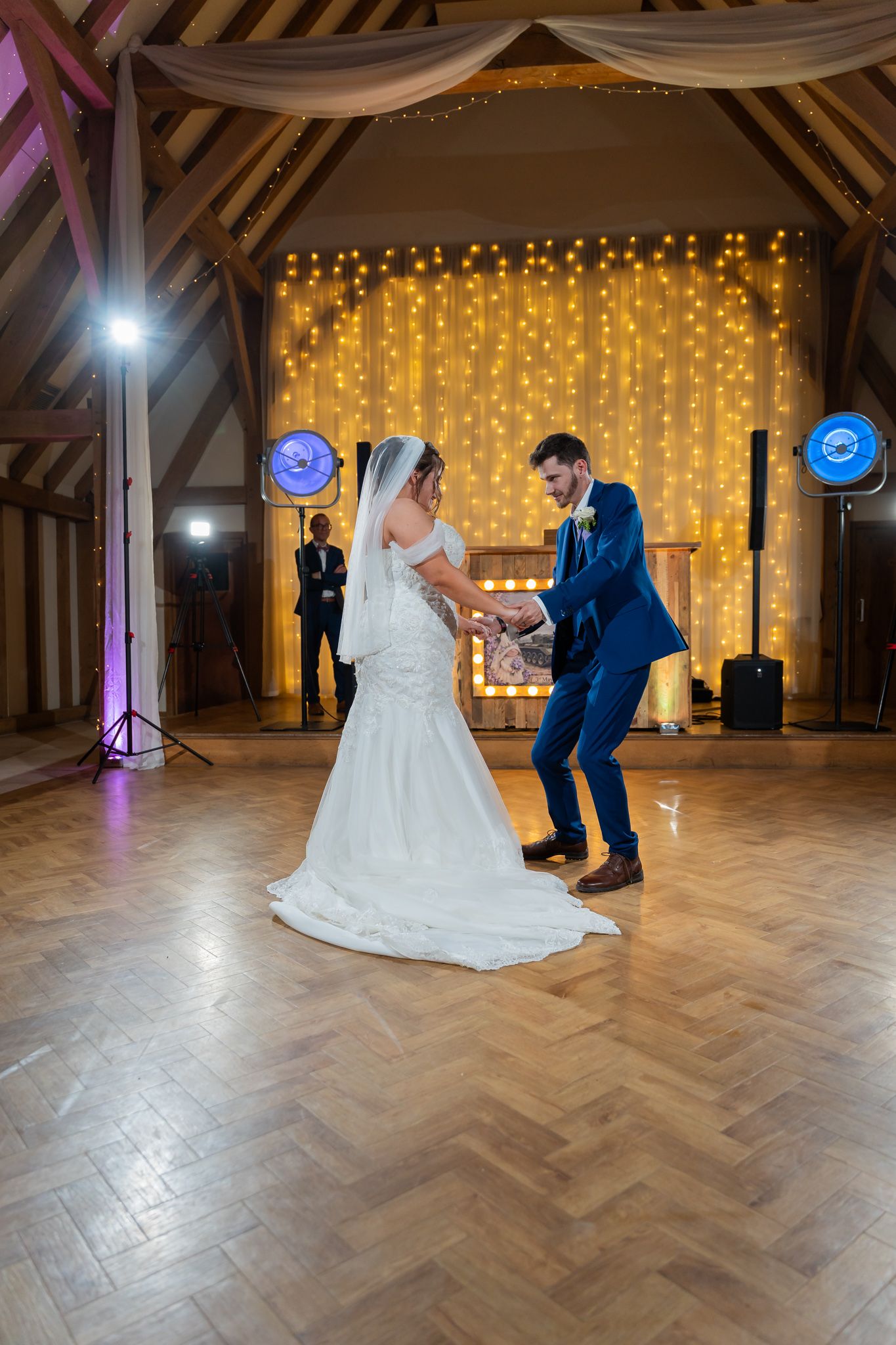 Bride and groom share their first dance in a rustic barn venue with warm fairy light backdrop.