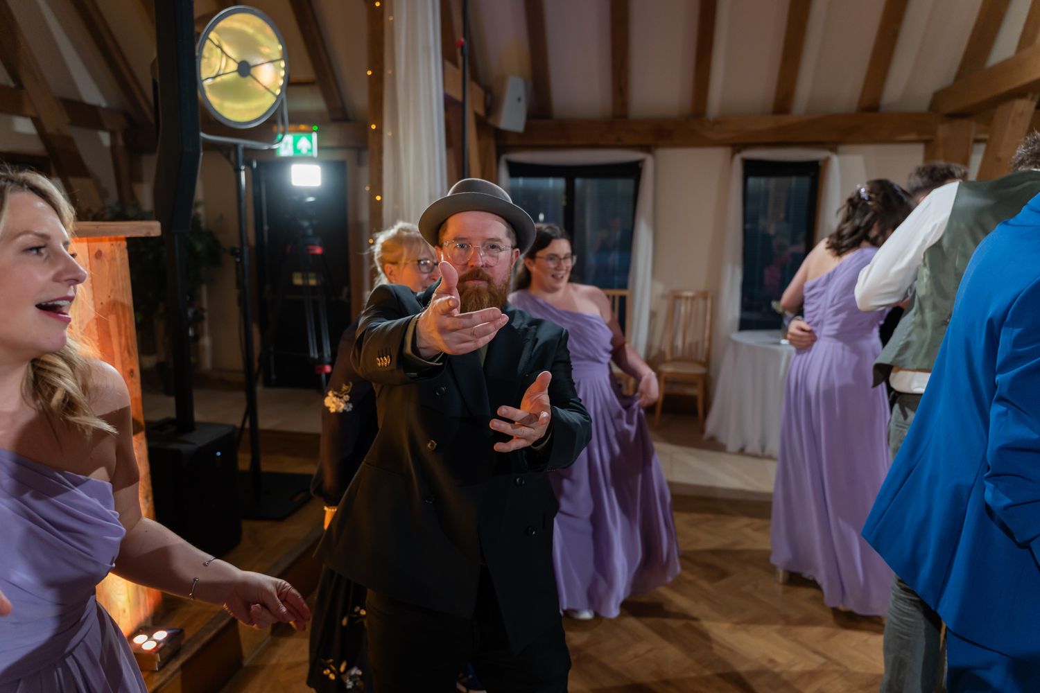 Guests dancing joyfully at a wedding reception in a rustic venue with purple bridesmaid dresses.