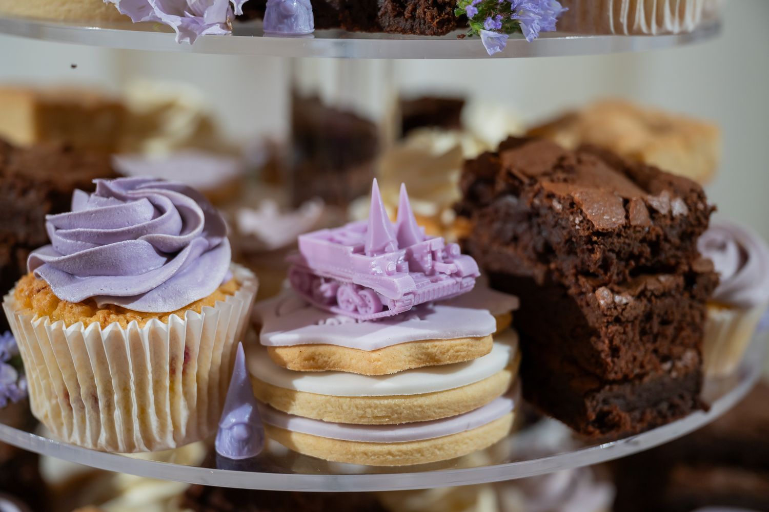 Elegant tiered dessert stand with purple frosted cupcakes, iced cookies, and rich chocolate brownies for a special occasion.