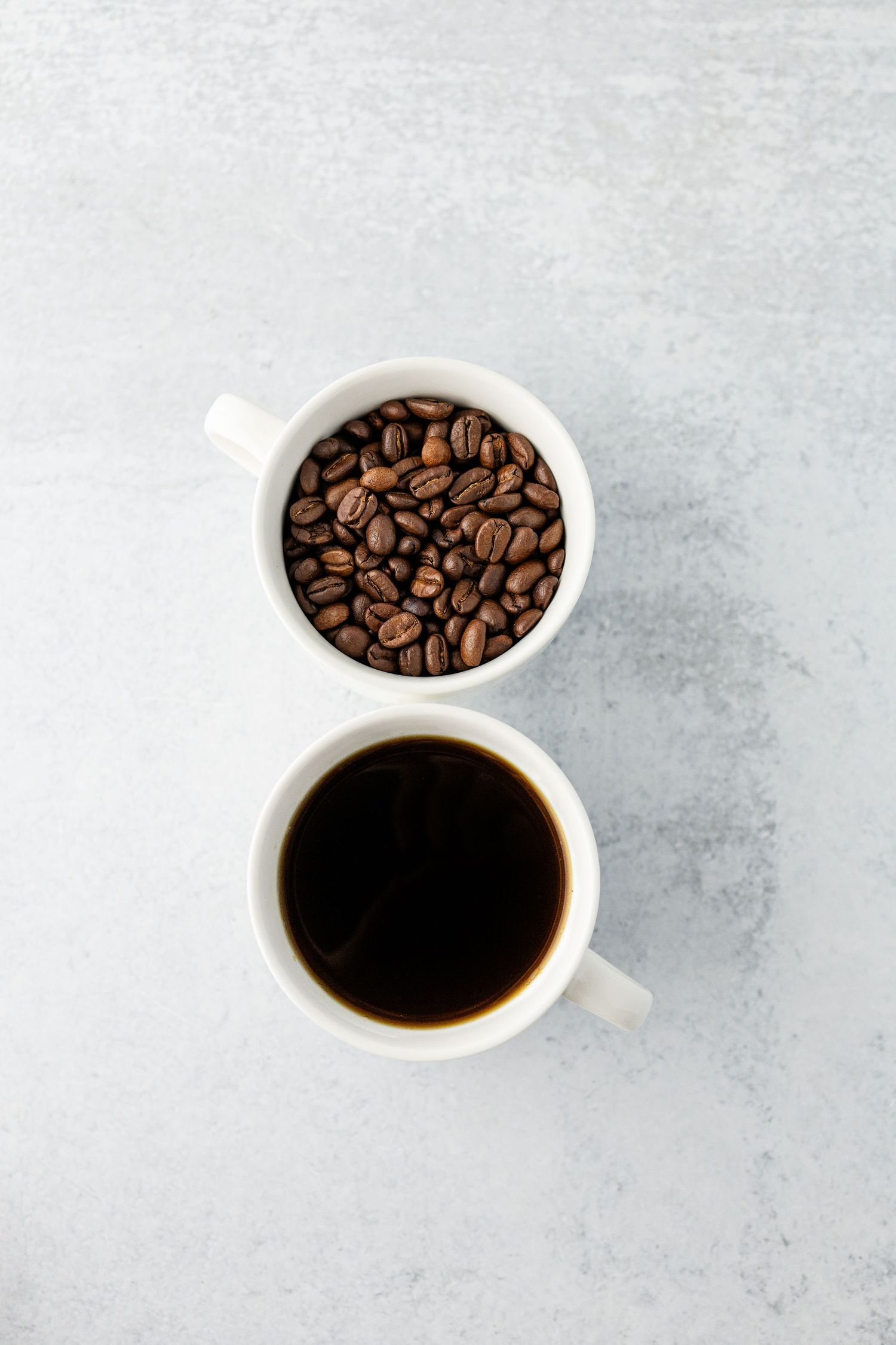 Hero shot of two white coffee cups filled with coffee beans and brewed coffee against a clean marble background.