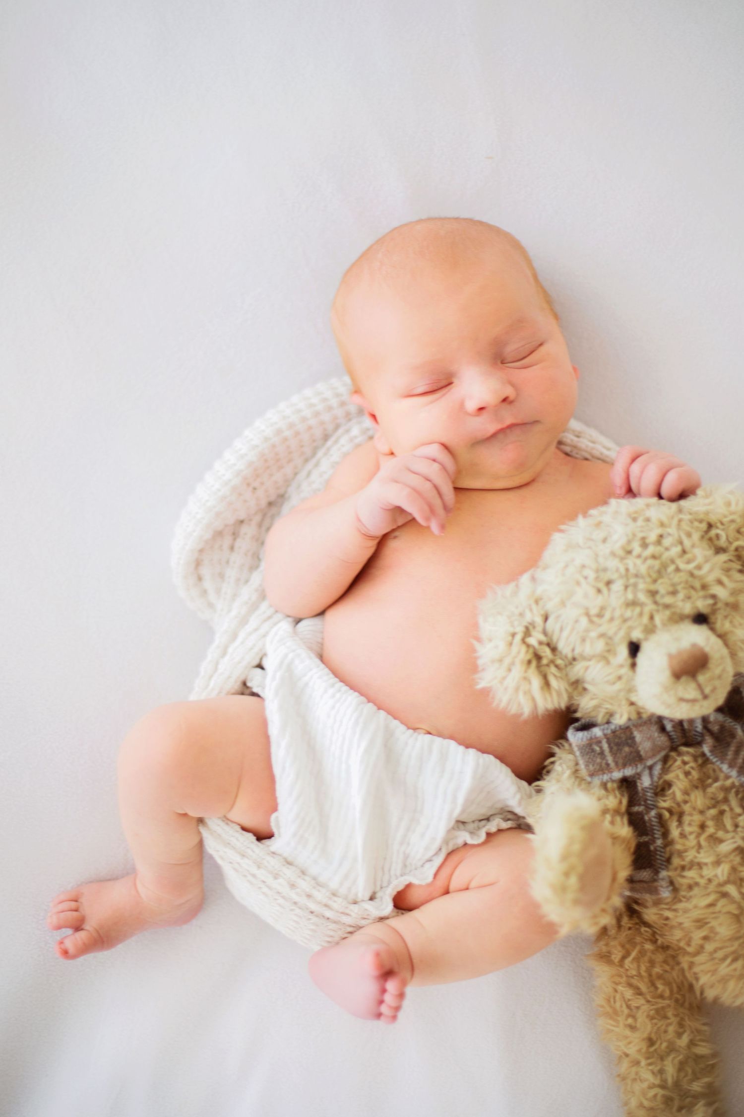 Peaceful newborn baby sleeping with a teddy bear on a white blanket.
