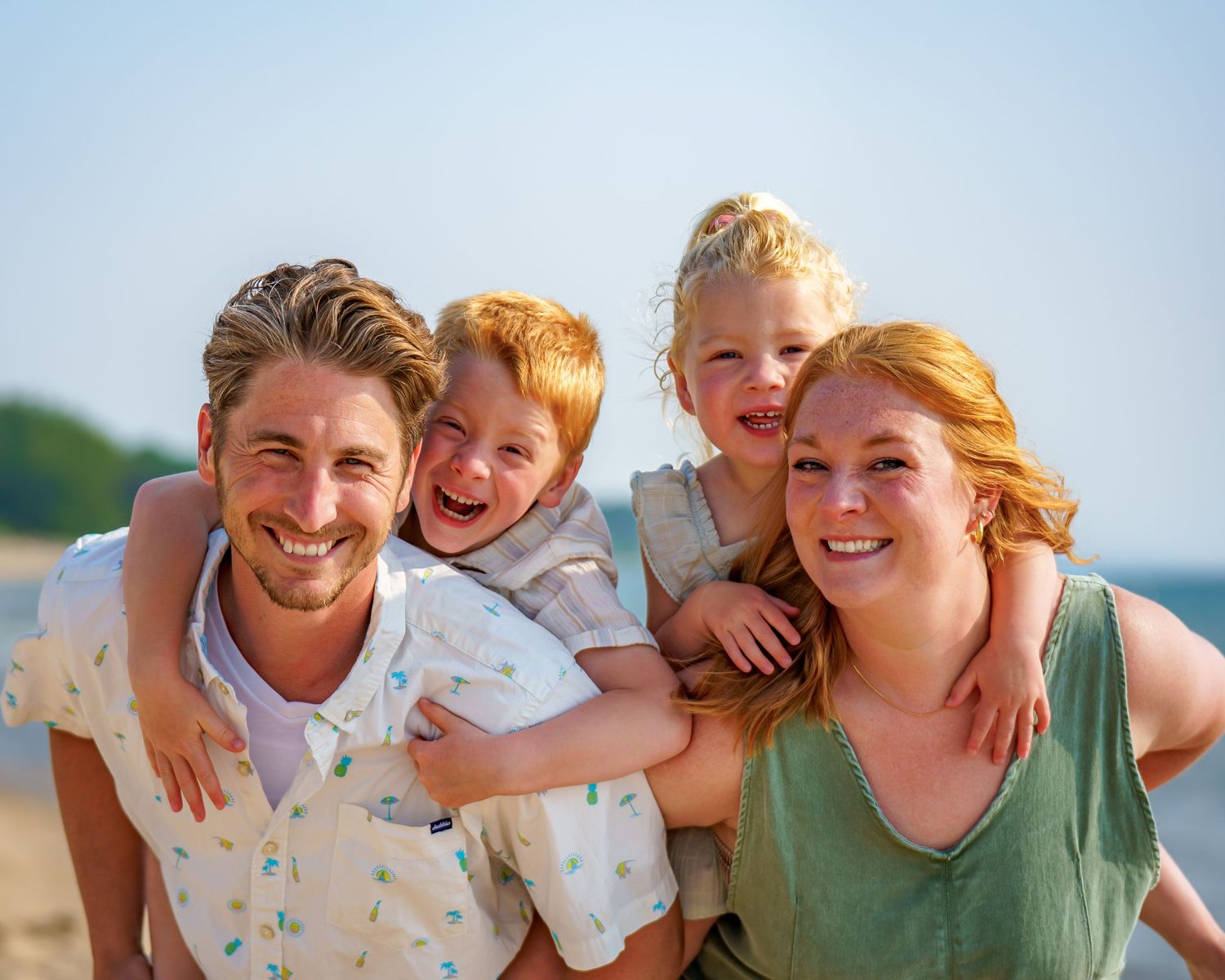 Happy family of four with red hair smiling at the beach on a sunny day.
