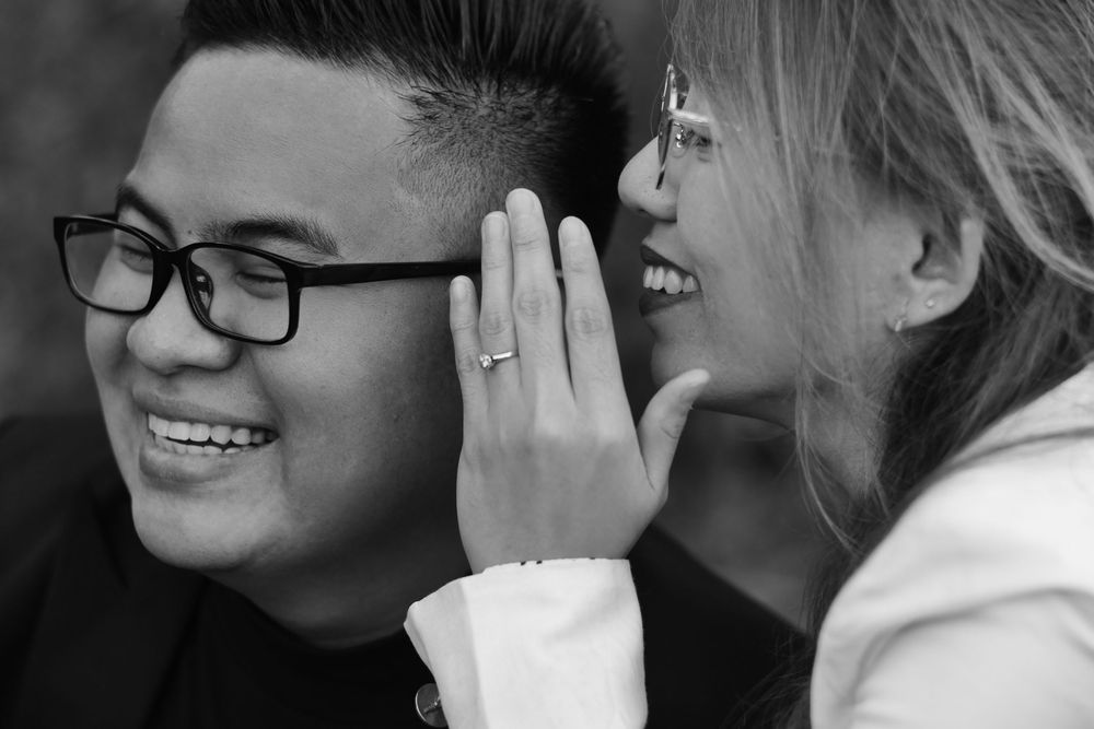 Black and white close-up of smiling couple, woman showing off engagement ring.