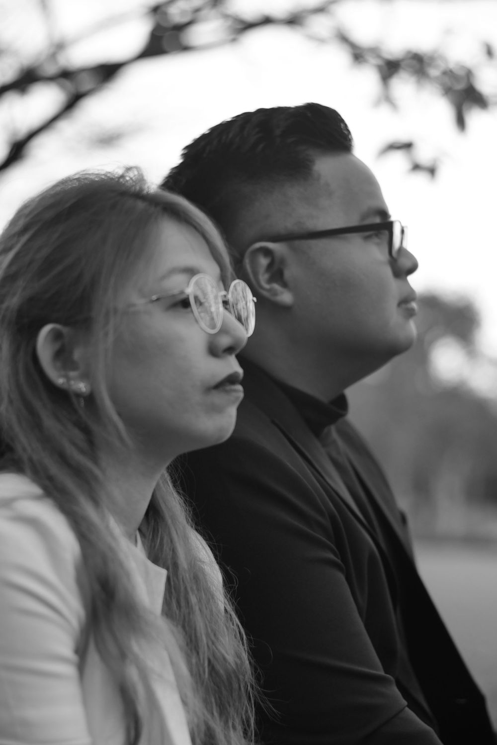Black and white profile portrait of couple sitting together wearing glasses outdoors.