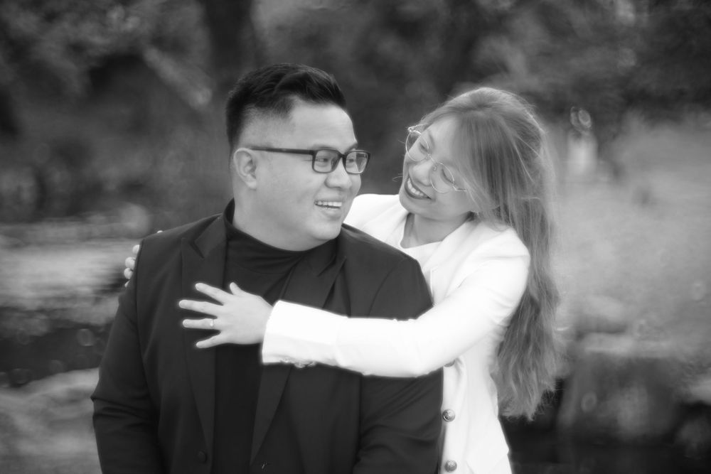 Black and white portrait of a laughing couple embracing outdoors in a natural setting.