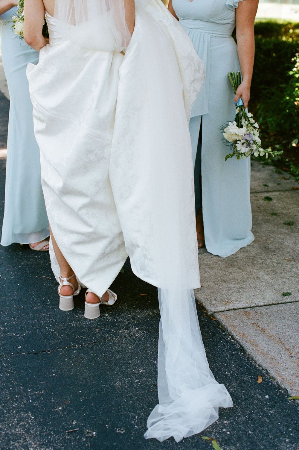 Bridesmaids in light blue gowns help lift bride's white wedding dress train.