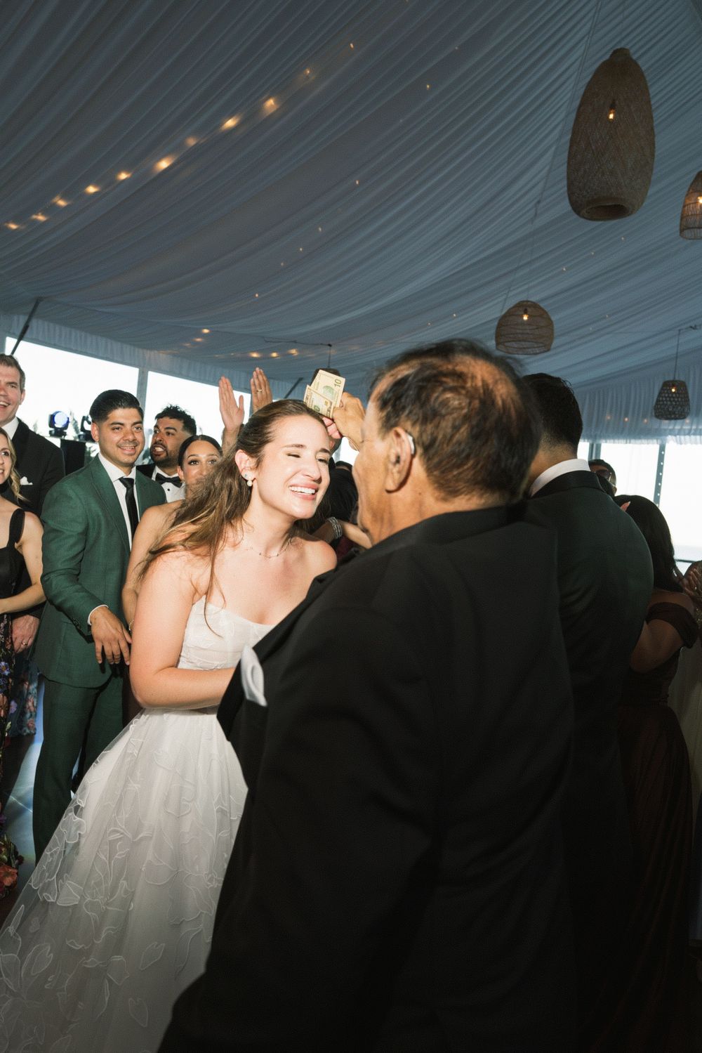 Bride smiling and dancing with guests at elegant wedding reception under draped ceiling.