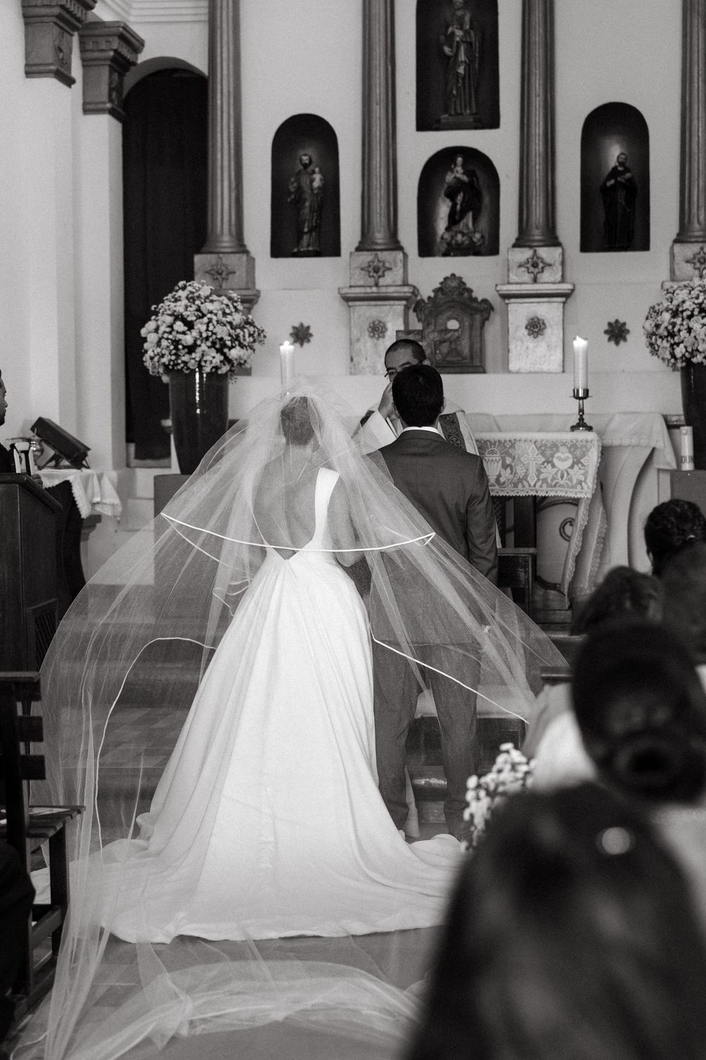 Bride in elegant gown with long veil walks toward altar with groom during church wedding ceremony.