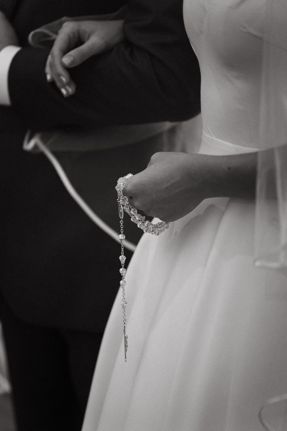 Bride holding delicate rosary beads in white gloved hands during religious wedding ceremony.