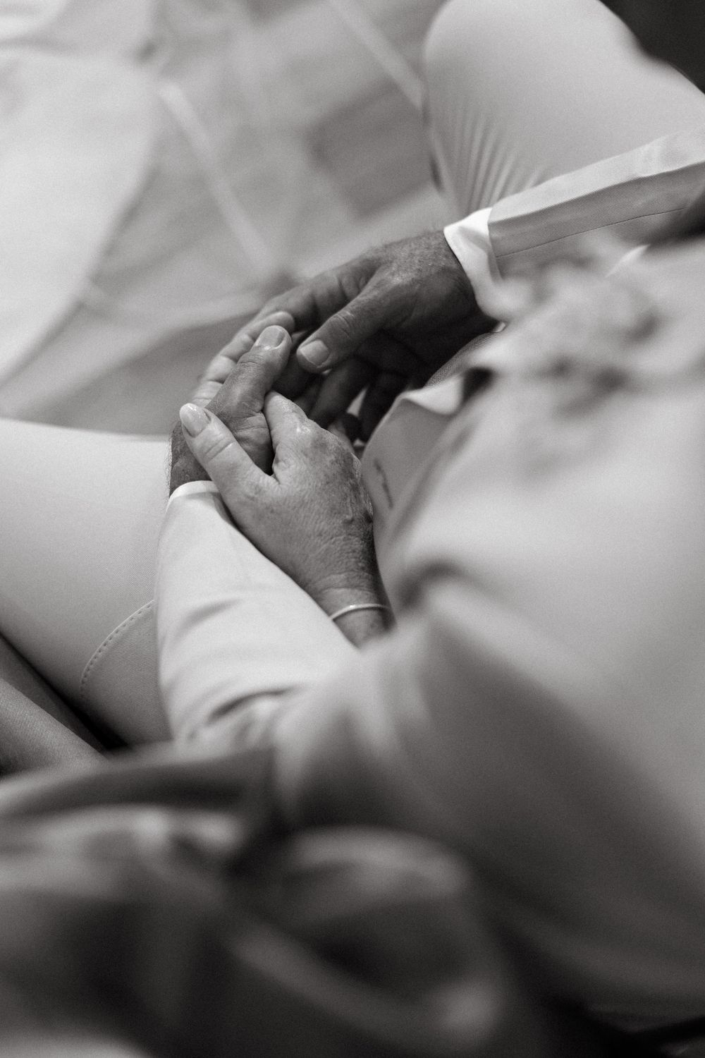 Close-up black and white photo of bride and groom holding hands tenderly during wedding ceremony.