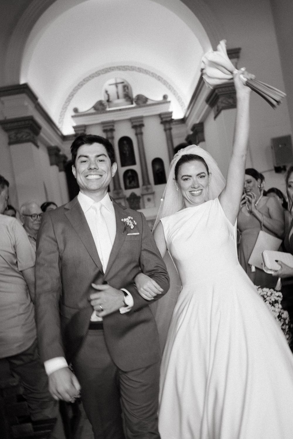 Joyful bride and groom exit church celebrating marriage, bride raising bouquet triumphantly in air.
