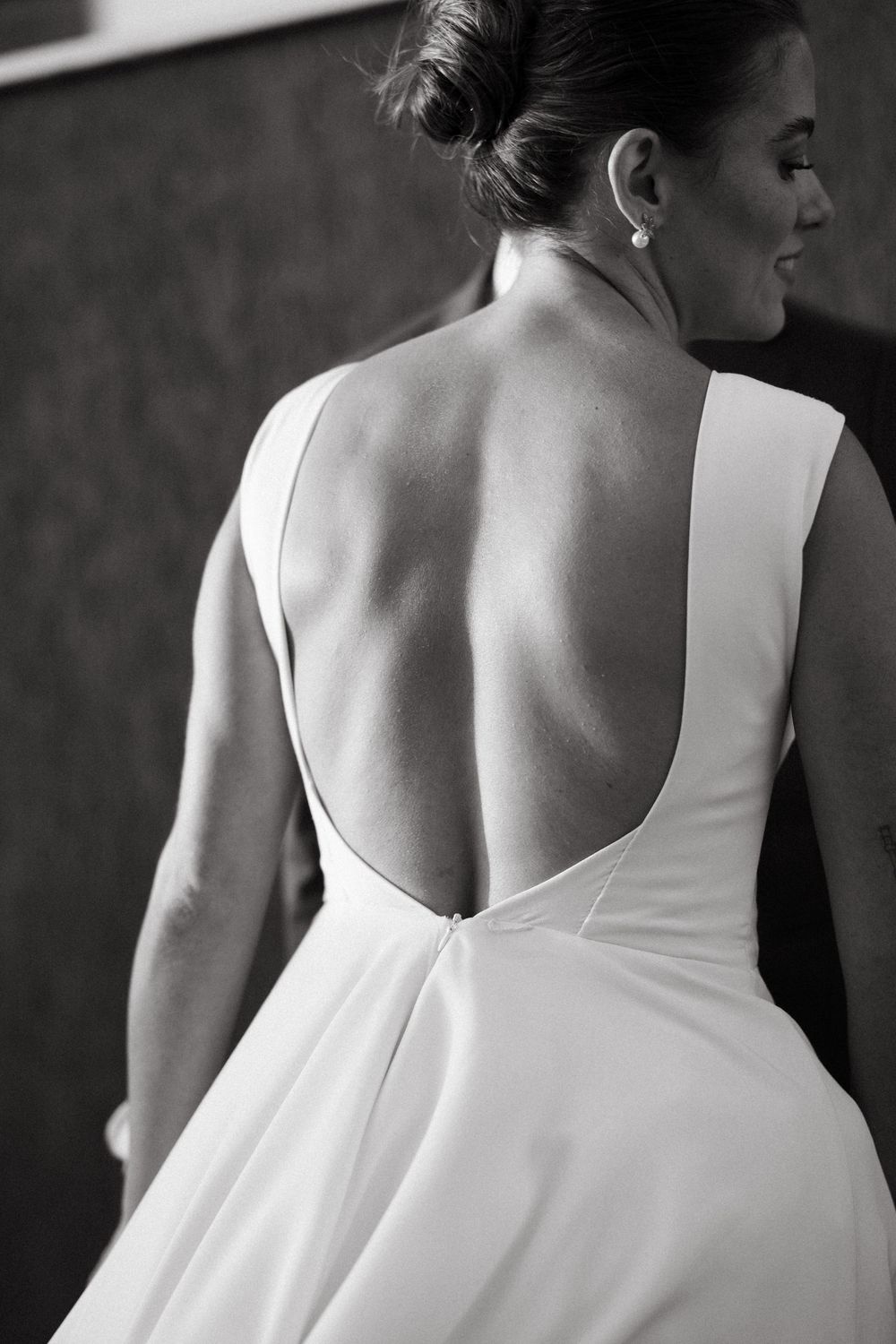 Elegant bride in open-back white wedding gown with pearl earring and updo hairstyle.