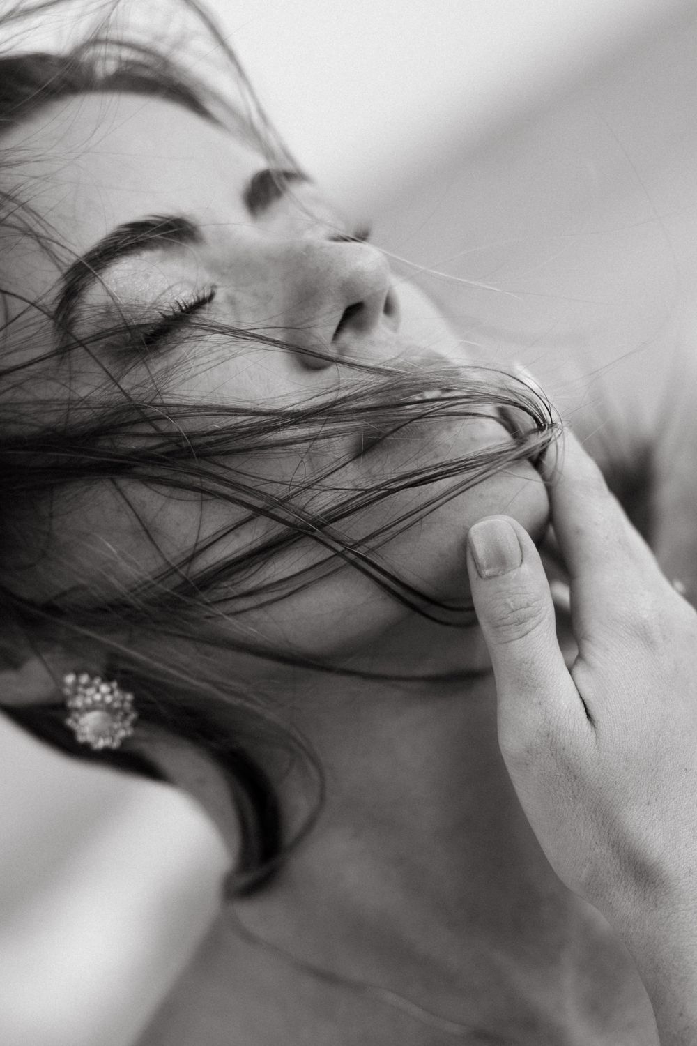 Black and white close-up of a woman with wind-blown hair being gently touched by a hand.