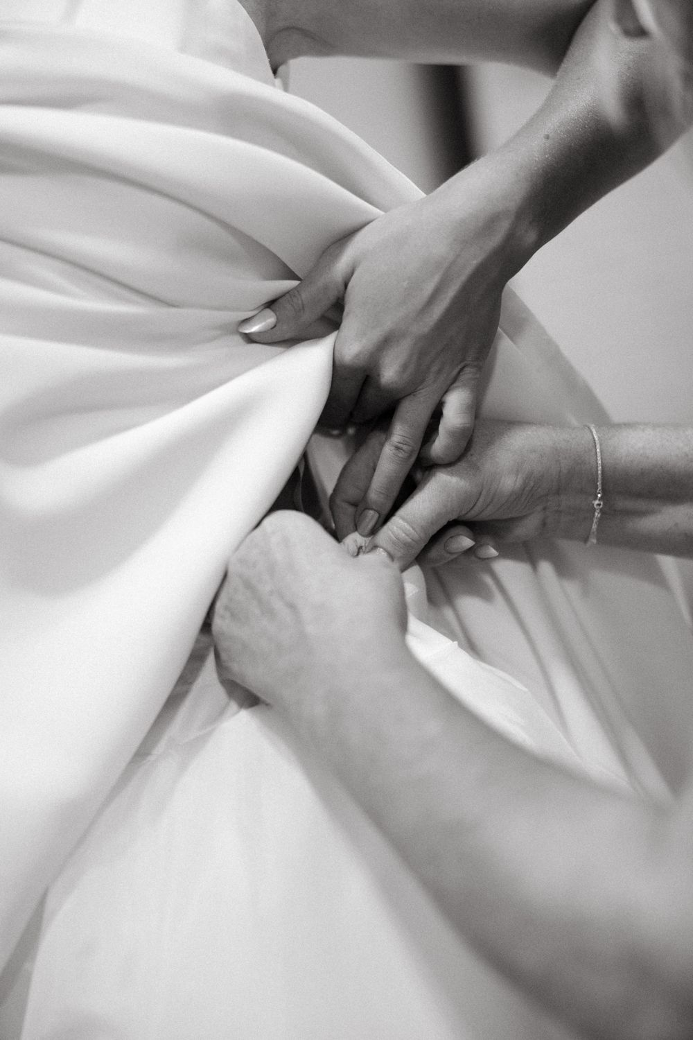 Multiple hands fastening buttons on back of brides white wedding gown before ceremony.