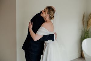 A bride in an off-shoulder gown and groom in navy suit share a tender embrace during their wedding day first look.