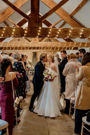 Bride and groom share a kiss at the altar in a rustic barn wedding venue adorned with fairy lights and wooden beams.