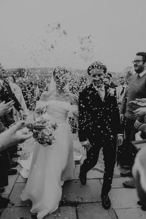 Newlyweds walk through a joyful confetti shower surrounded by cheering guests after their wedding ceremony.
