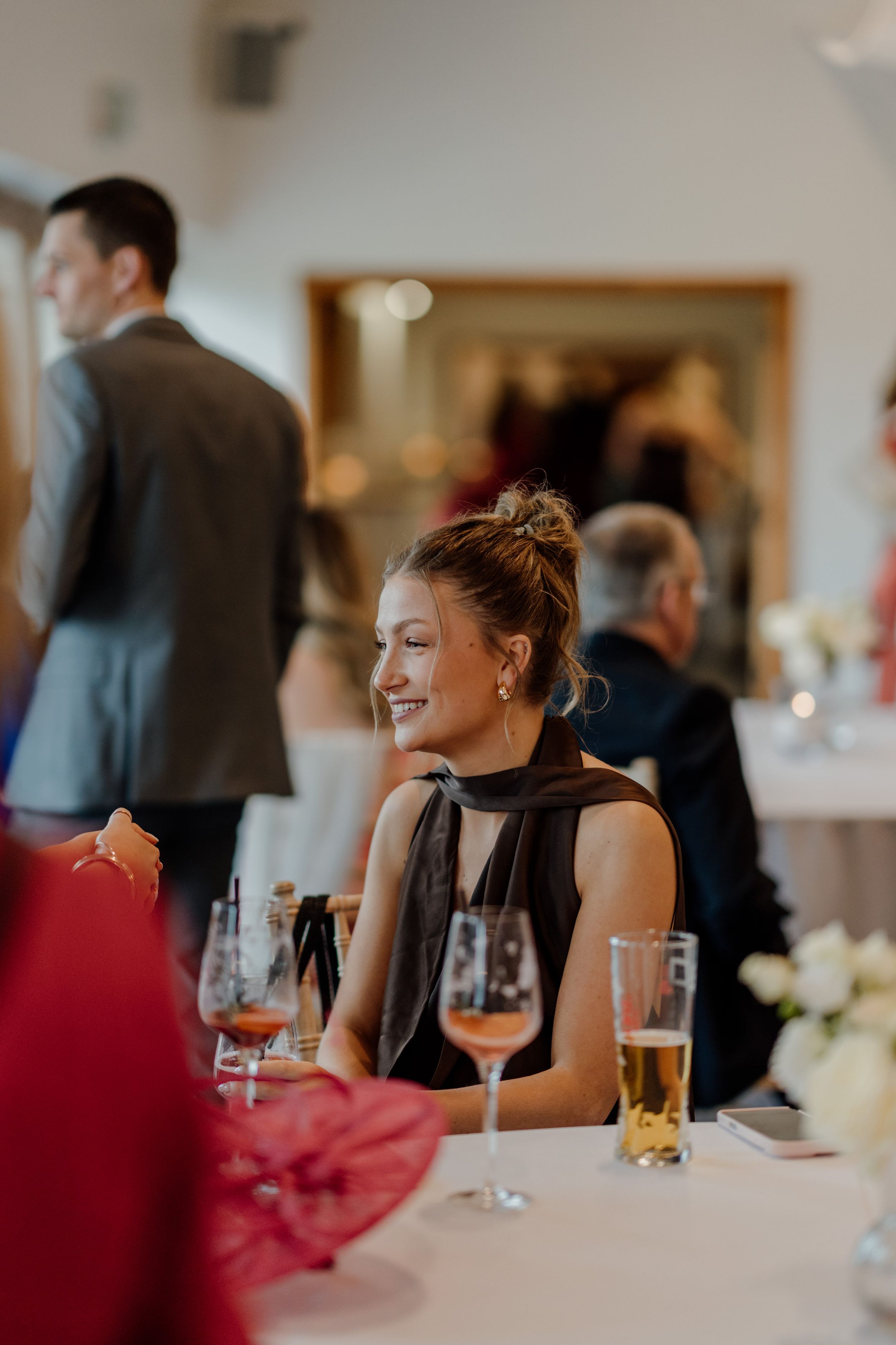 Smiling woman in black dress enjoying a wedding reception dinner with champagne glasses on the table.