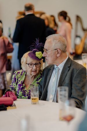 Elderly couple in formal attire share a moment at a wedding reception table.