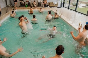 Group of men splashing and playing in an indoor swimming pool during a lively party celebration.