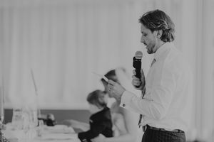 Black and white photo of a man in white suit delivering a speech at a wedding reception.