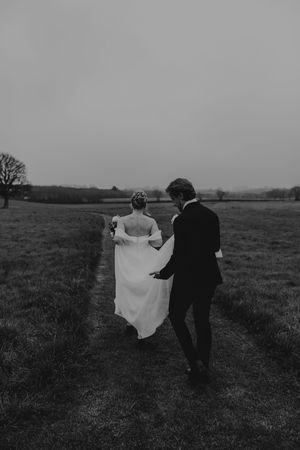 Bride and groom walking hand in hand across a misty field in black and white wedding photo.
