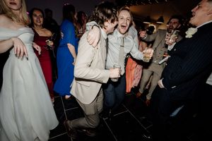 Two guests laughing and dancing joyfully at a wedding reception on a black dance floor.