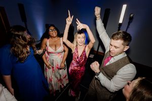 Wedding guests dance energetically under blue lights at a lively reception party.