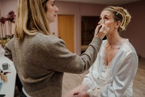 Professional makeup artist applying makeup to a bride in a white robe before her wedding.
