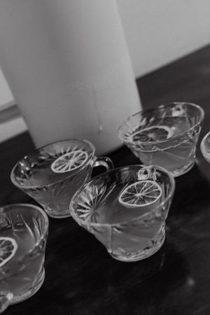 Black and white photo of elegant crystal punch cups with lemon slices beside a white pitcher.