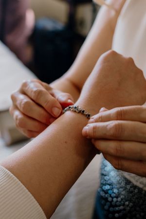 Helper fastening a delicate crystal bracelet on the bride's wrist during wedding preparations.