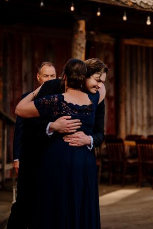 Emotional wedding guest in navy lace dress shares a heartfelt hug during a rustic barn reception.