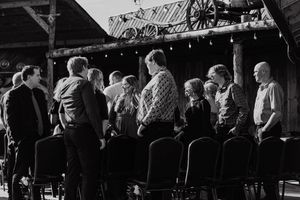 Group of people socializing outdoors near rustic wooden stage in black and white photo.