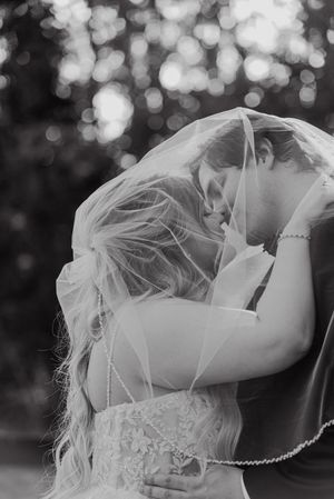 Bride and groom share an intimate moment under a veil in a romantic black and white wedding photo.