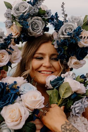 Smiling bride surrounded by blue, white, and gray rose floral arrangement on her wedding day.