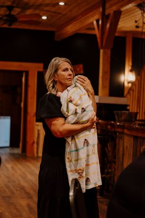 Woman in black dress tenderly holding a newborn baby wrapped in a colorful blanket indoors.