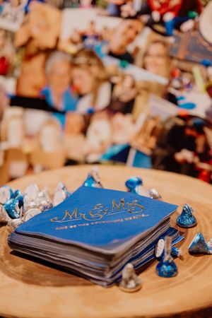 Blue Mr. & Mrs. wedding napkins surrounded by Hershey Kisses on wooden table with photo display backdrop.