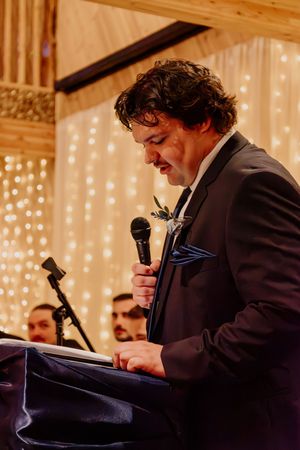 Groom delivers heartfelt wedding speech at podium with twinkling fairy lights in the background.