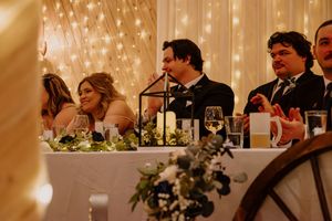 Bride and groom seated at decorated head table during wedding reception with candlelight centerpieces.