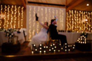 Blurred romantic wedding reception with fairy lights and couple celebrating on stage.