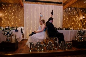 Bride and groom sit back-to-back at sweetheart table with Mr & Mrs marquee letters and fairy light backdrop.