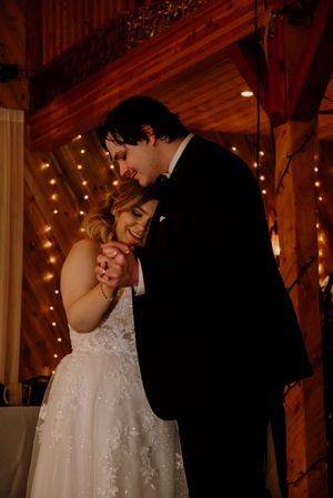Bride and groom share an intimate first dance in a rustic barn wedding venue adorned with warm string lights.