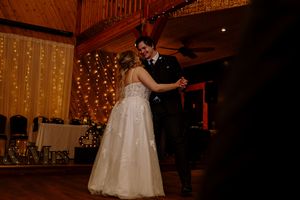 Bride and groom share first dance in rustic barn venue adorned with warm fairy lights.