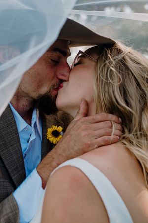 Bride and groom sharing a kiss under veil, groom wearing sunflower boutonniere.