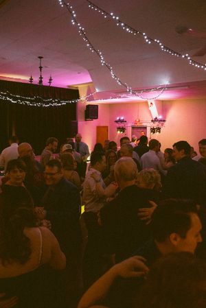 Guests dancing at a festive indoor event with warm pink lighting and twinkling fairy lights decorating the ceiling.