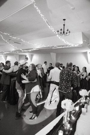 Black and white photo of guests dancing at an elegant indoor reception with fairy lights strung across the ceiling.