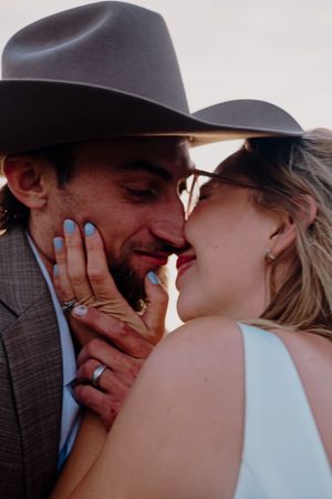 Couple in cowboy hats share a romantic close moment with wedding rings visible.